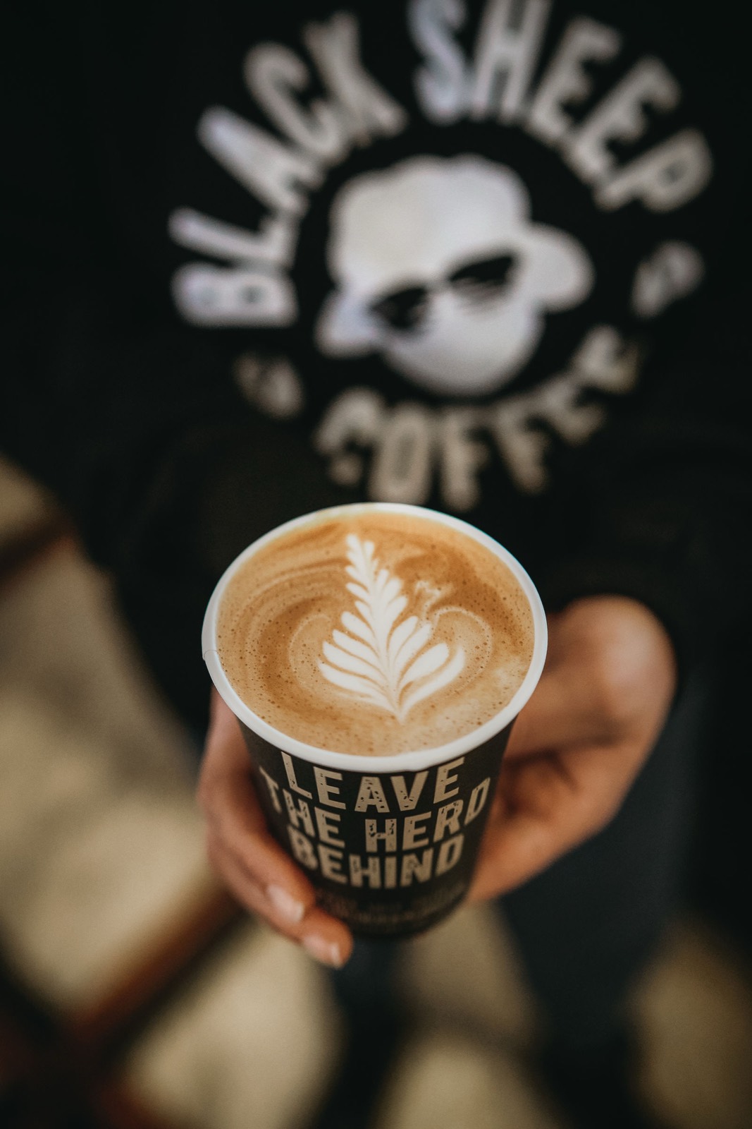 A latte in a Leave The Herd Behind cup, the brand mark facing camera.