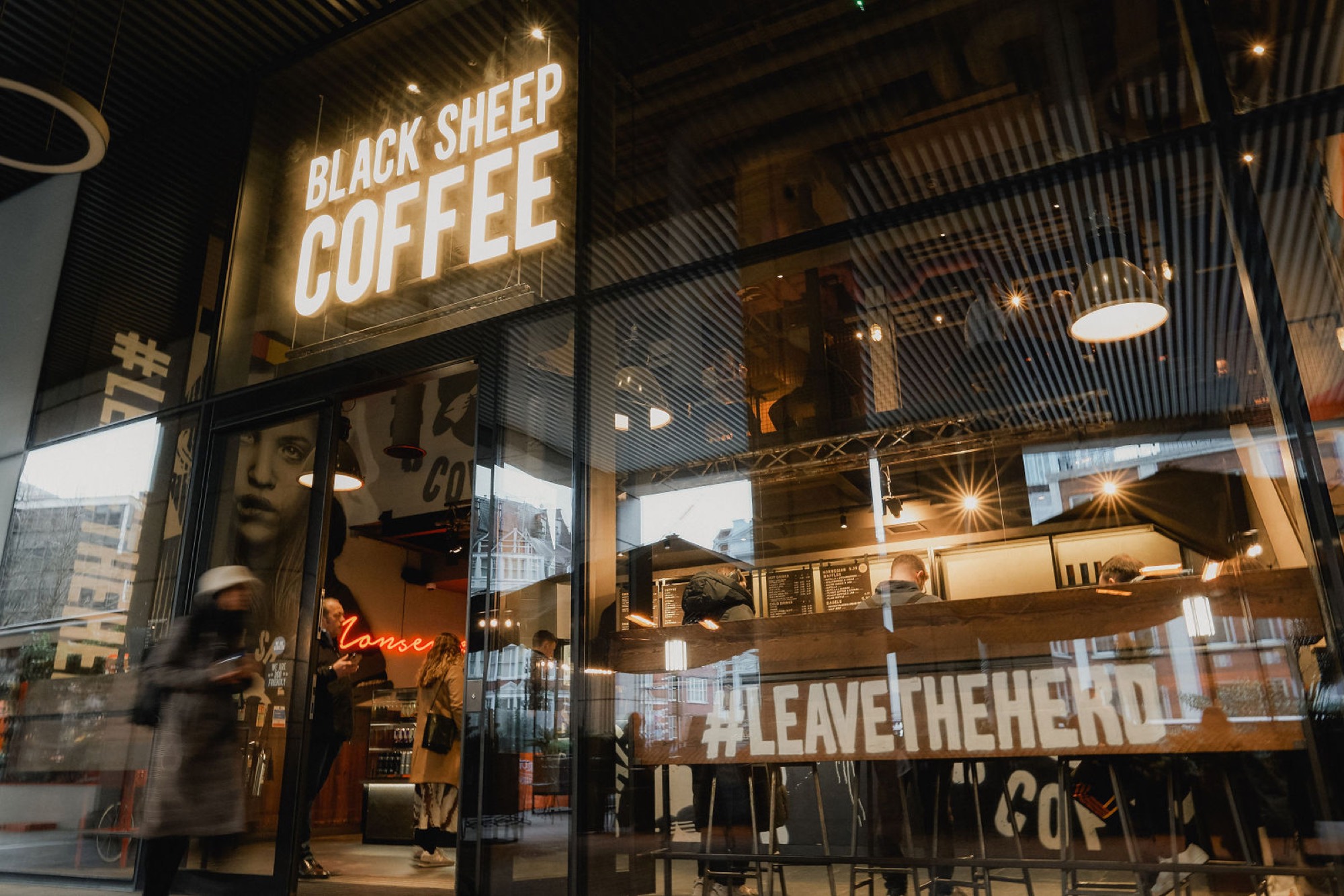 A Black Sheep Coffee storefront lit at dusk, manifesto graphics across the window.