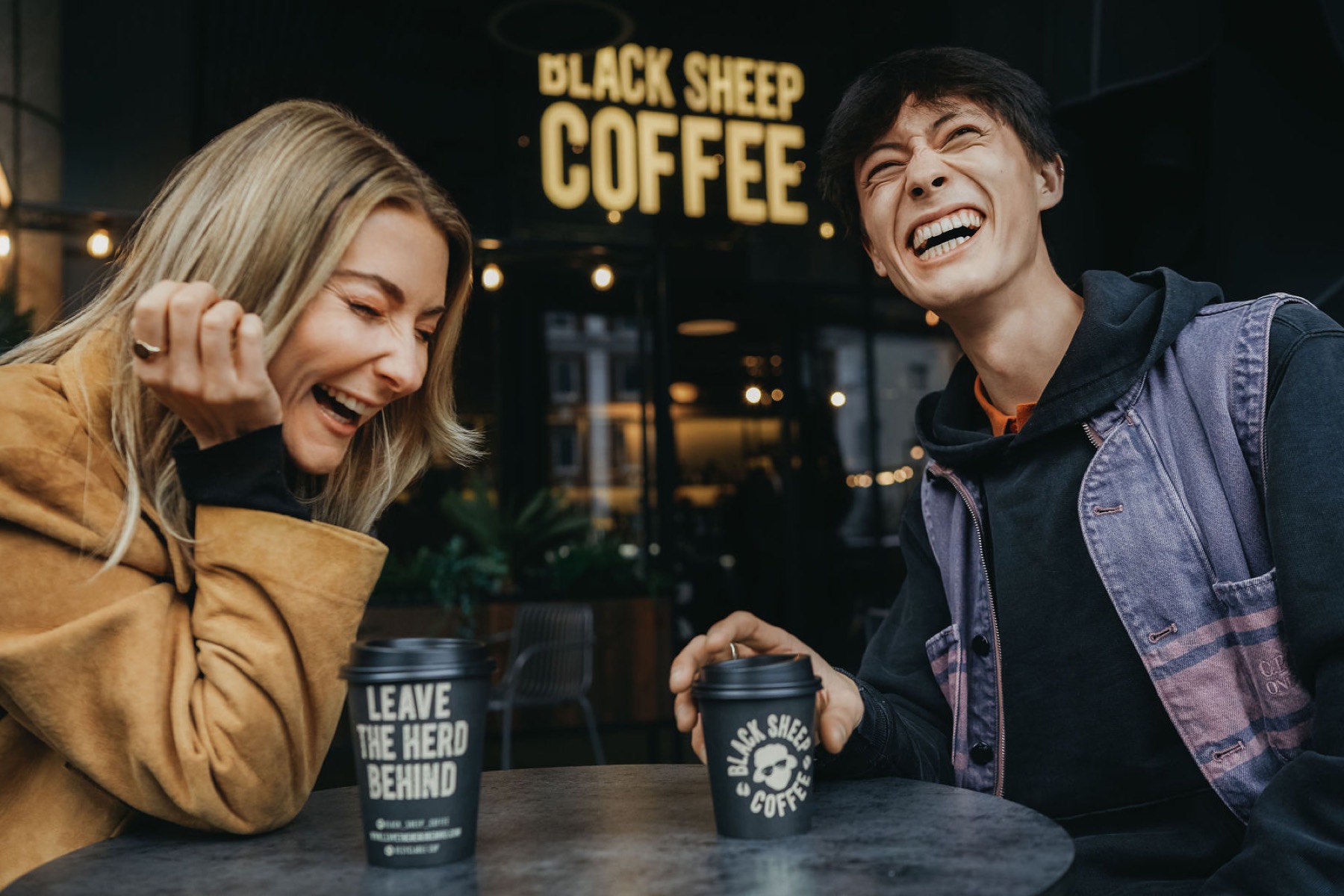 Two customers laughing at a table beneath the Black Sheep sign.