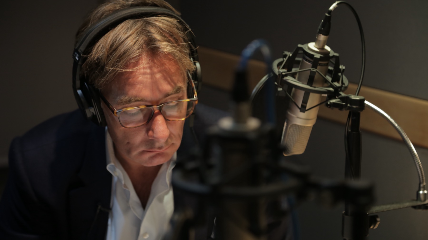 Christian recording in a studio, headphones on, condenser microphone in frame.