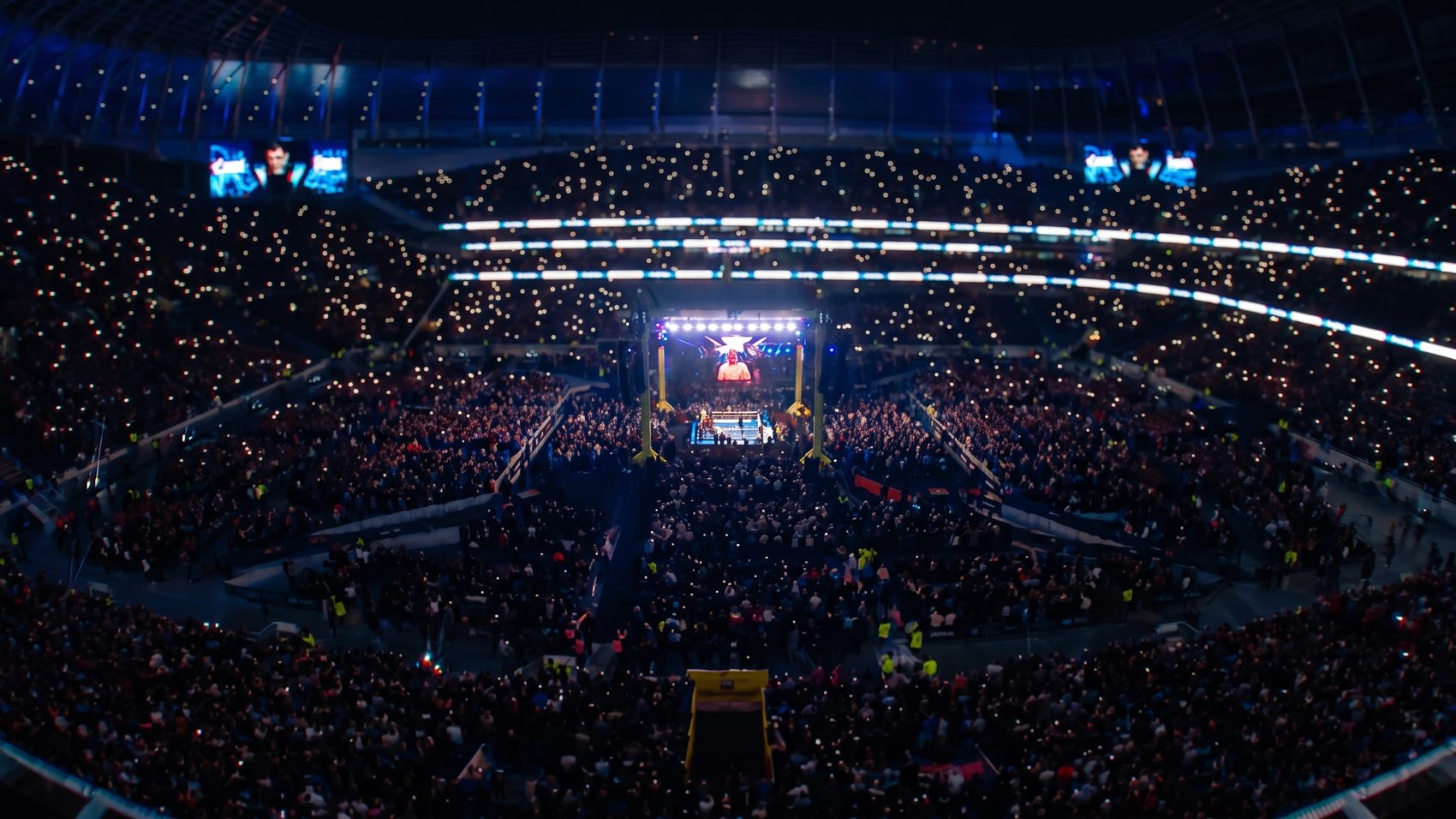A stadium bowl in the dark, phone lights across every tier.