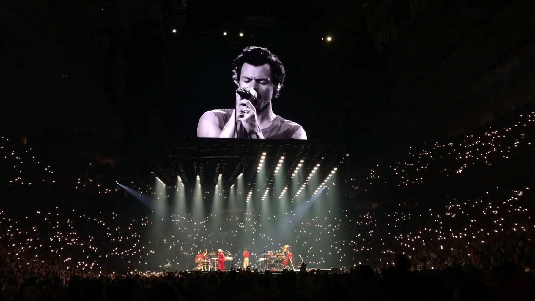 An arena on tour, the crowd lit end to end, the band small on a wide stage.