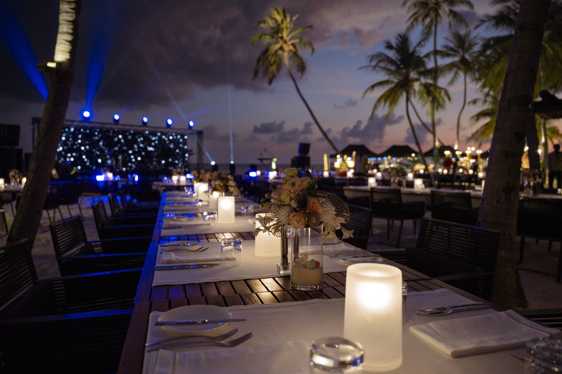 A long candlelit table set down the deck at dusk.